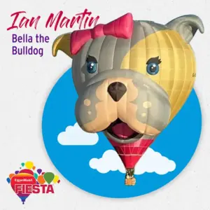 A balloon shaped like a bulldog with a bow, against a blue, cloudy backdrop featuring the ExxonMobil Fiesta logo.