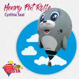 A hot air balloon shaped like a cartoon seal floats against a circular cloud backdrop. It's part of the ExxonMobil Fiesta event.