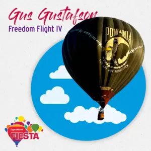 A black hot air balloon with a POW*MIA design floats against a blue sky with clouds illustration, promoting ExxonMobil Fiesta event.