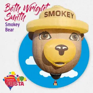 A large Smokey Bear hot air balloon with a yellow hat, displayed at the ExxonMobil Fiesta event, with a clear blue sky backdrop.