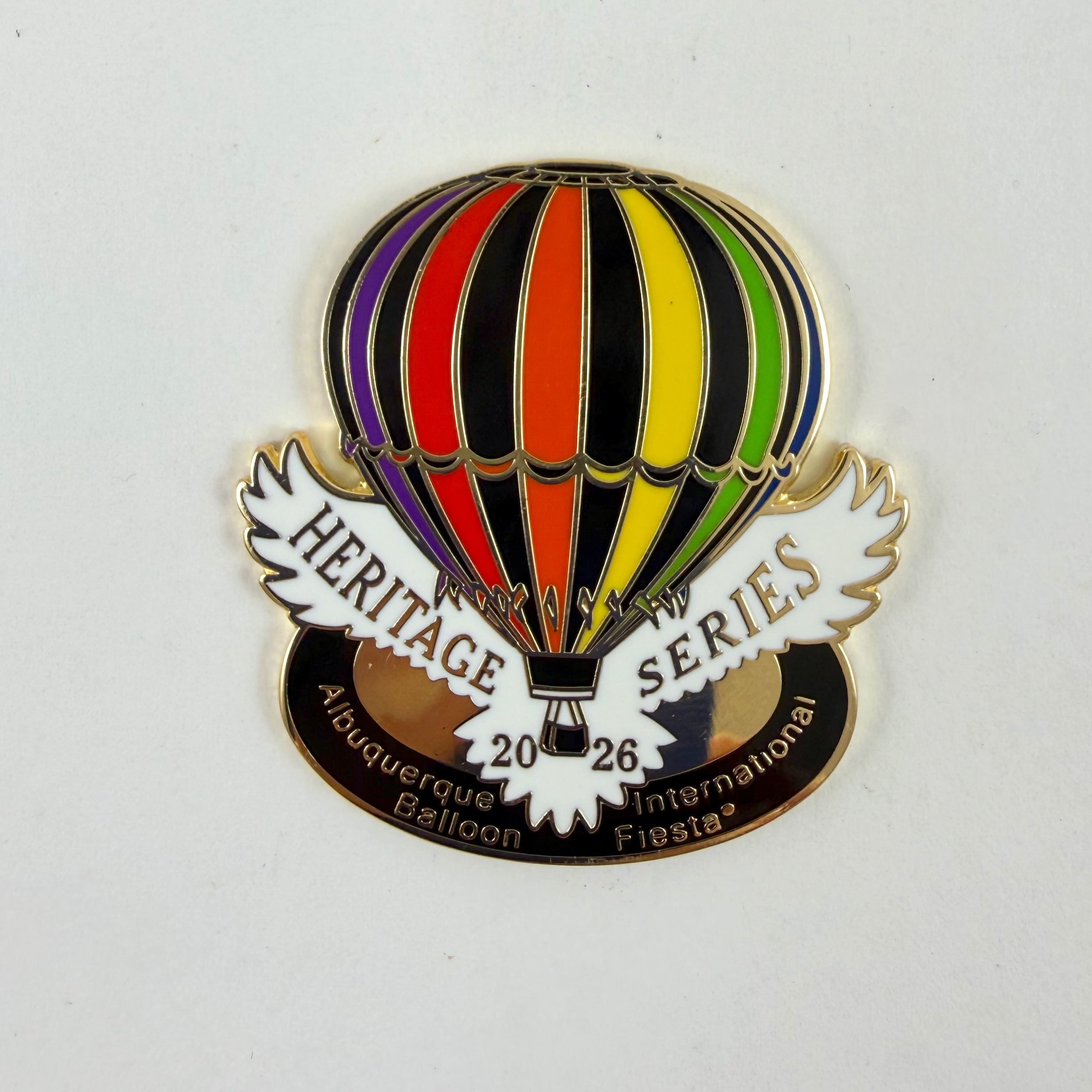 IMG_5248 Colorful hot air balloon pin with "Heritage Series 2025" on wings. Text reads "Albuquerque International Balloon Fiesta." Bright design, festive theme.