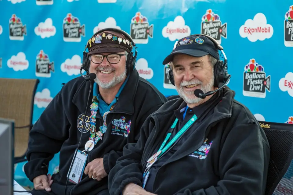 balloon-fiesta-live-broadcasters03 Balloon Fiesta Live broadcasters wearing headsets, smiling at a media event with ExxonMobil and Balloon Fiesta Live banners in the background.