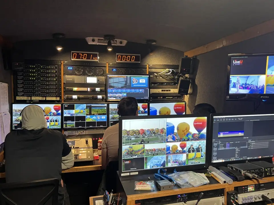 balloon-fiesta-live-control-room Balloon Fiesta Live control room with three people monitoring various screens displaying live footage of hot air balloons and events.