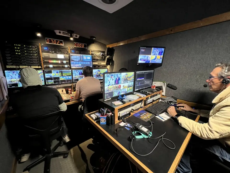 balloon-fiesta-live-control-room02 Three people operate multiple screens and equipment in the Balloon Fiesta Live control room. Headsets and monitors display various video feeds for broadcast production.