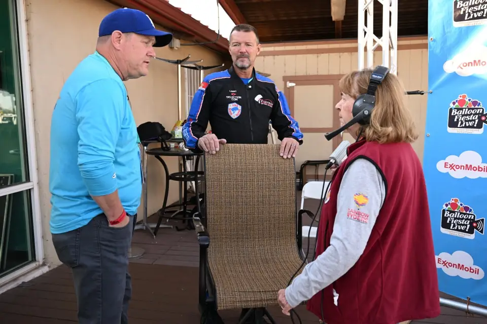 balloon-fiesta-live-staff-with-balloonmeister Three people are gathered, wearing casual and event-themed clothing. One person wears a headset. Background shows "Balloon Fiesta Live!" signage.