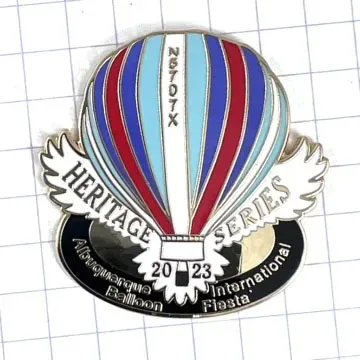 A colorful hot air balloon pin from the 2023 Albuquerque International Balloon Fiesta, featuring the "Heritage Series" label on grid paper.