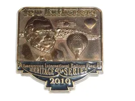 2010-Honoree-Tom-Rutherford A pin featuring a person, hot air balloons, and "Albuquerque International Balloon Fiesta Heritage Series 2010" inscription, set against a mountainous backdrop.