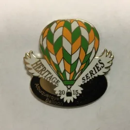 2015-Honoree-Dick-Rice Hot air balloon pin labeled "Heritage Series 2015" with "Albuquerque Balloon" inscribed inside black oval. Balloon features green, orange, white pattern.