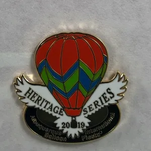2019-Honoree-George-Hahn Colorful hot air balloon pin from Albuquerque International Balloon Fiesta 2019, labeled "Heritage Series," with decorative wings beneath the balloon.